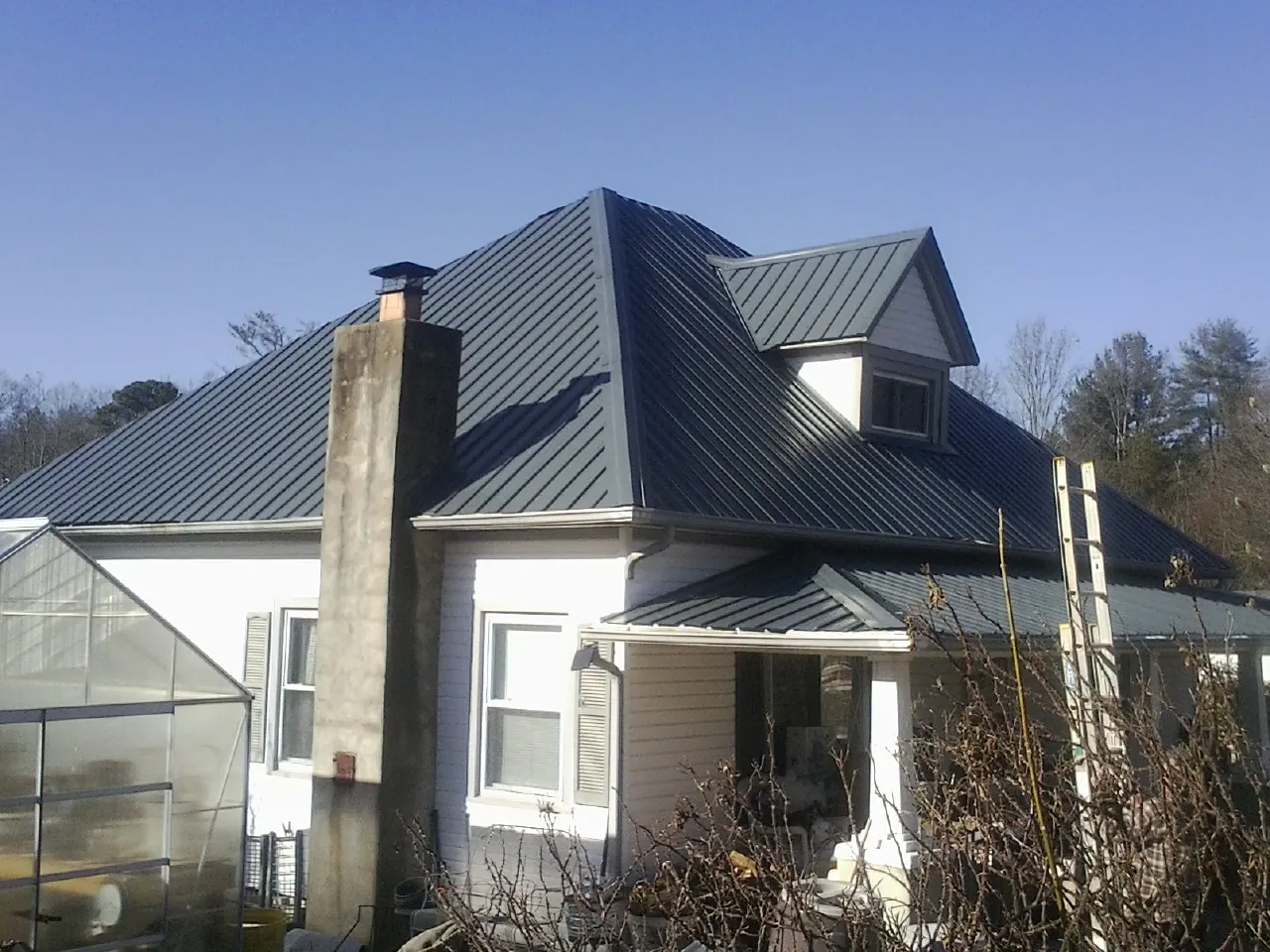 Dark blue standing seam metal roof on a white farmhouse with dormer — Slate & Tile Roof Repair by Roofing Brothers in Gulf