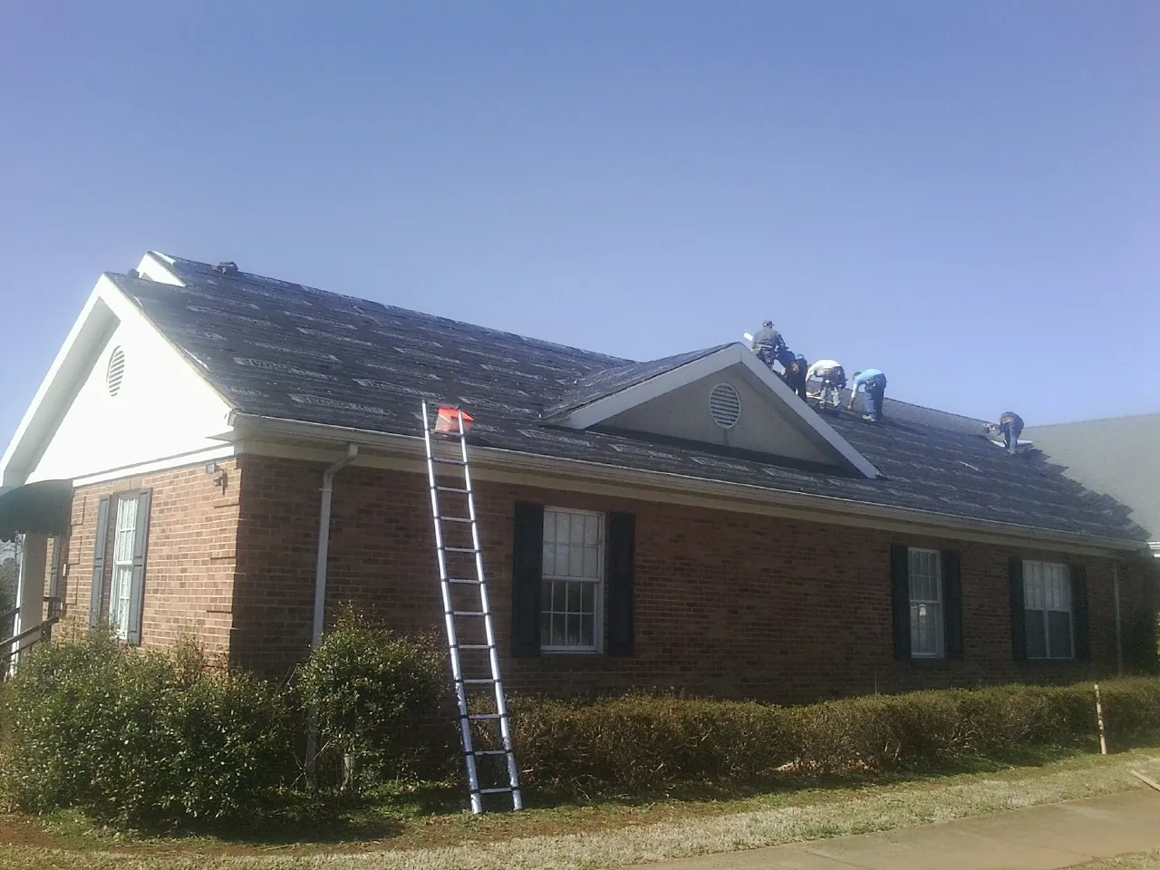Crew tearing shingles off a brick ranch roof with a ladder set — Metal Roof Repair work by our crew in Gulf
