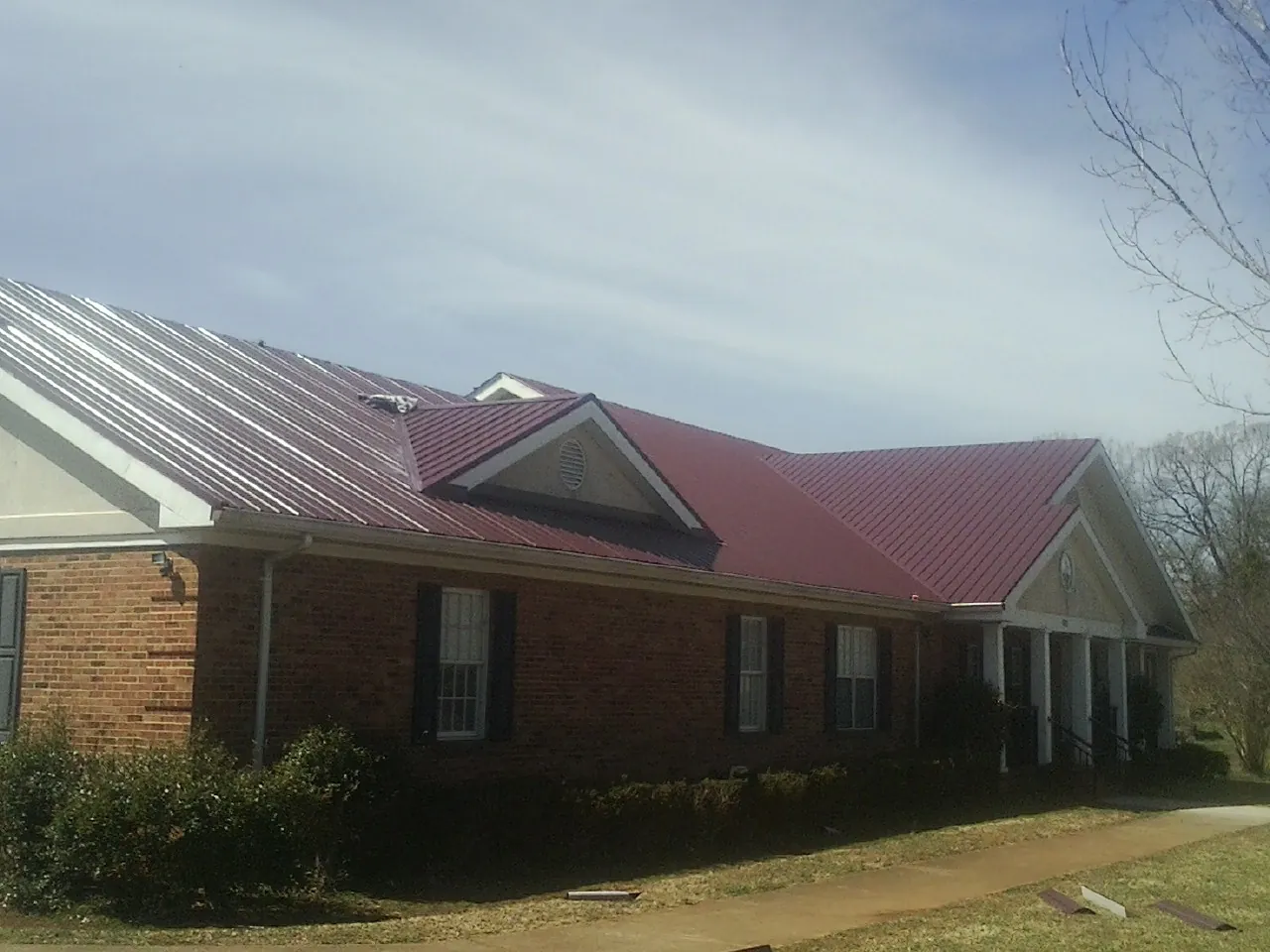Red metal roof with gabled entries on a long brick building, from a Hail Damage Roof Repair job in Gulf