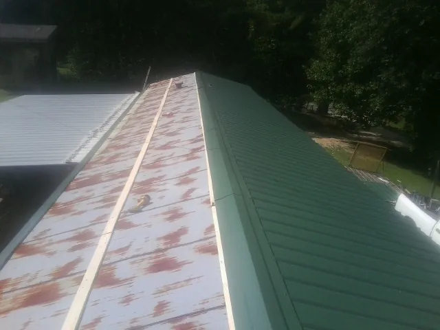 Old rusted panels beside newly installed green metal roofing — Wind Damage Roof Repair by Roofing Brothers in Gulf