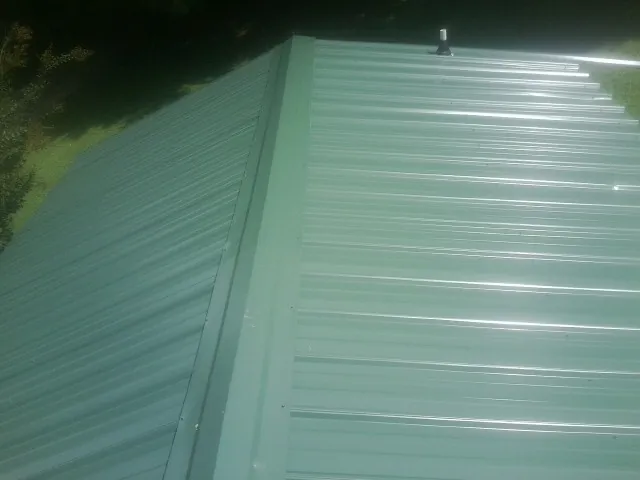 New green metal panels meeting at the ridge of a roof — Flat Roof Repair work by our crew in Gulf
